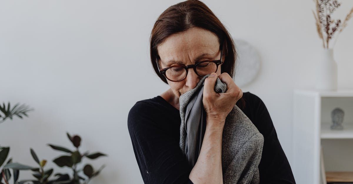 A woman with glasses holding a cloth to her face while grieving