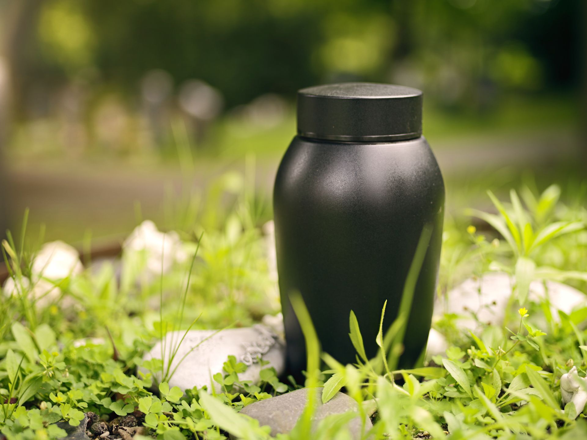 A dark cremation urn standing in green grass