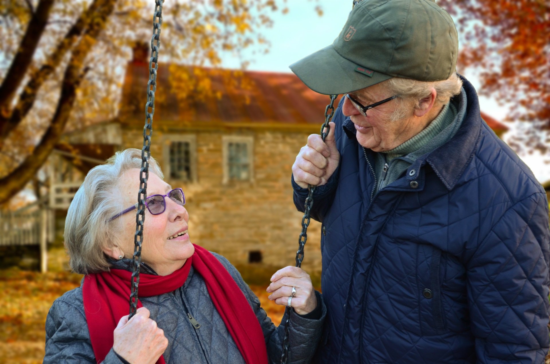 An older woman and man on a swing in front of a house in autumn